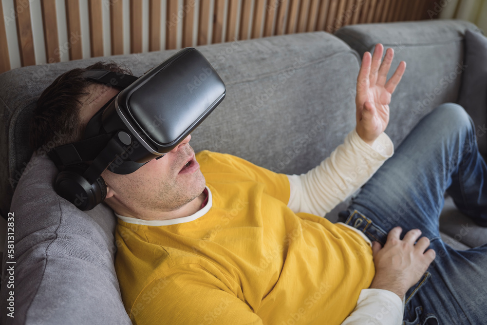 a man watching a video in virtual reality glasses lying on the couch at home.. People and technology metaverse concept. 360 degree video viewing