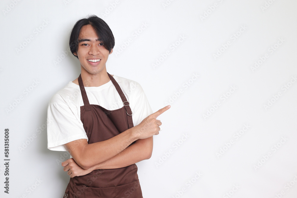 Portrait of attractive Asian barista man in brown apron showing product, pointing at something with hands. Advertising concept. Isolated image on white background Portrait of attractive Asian barista man in brown apron showing product, pointing at something with hands. Advertising concept. Isolated image on white background