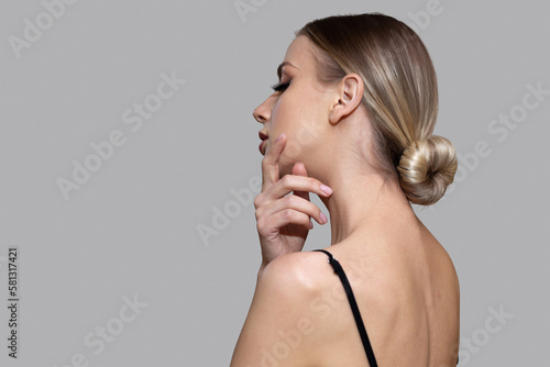Woman with bun hairstyle on gray background. Bare back, shoulders and neck. Back view photo