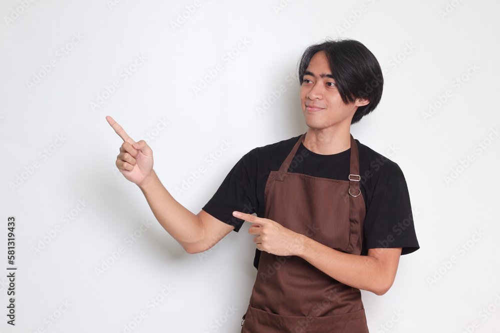 Portrait of attractive Asian barista man in brown apron showing product, pointing at something with hands. Advertising concept. Isolated image on white background Portrait of attractive Asian barista man in brown apron showing product, pointing at something with hands. Advertising concept. Isolated image on white background