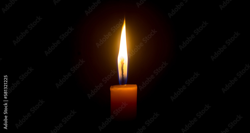 A single burning candle flame or light glowing on an orange candle on black or dark background on table in church for Christmas, funeral or memorial service with copy space A single burning candle flame or light glowing on an orange candle on black or dark background on table in church for Christmas, funeral or memorial service with copy space