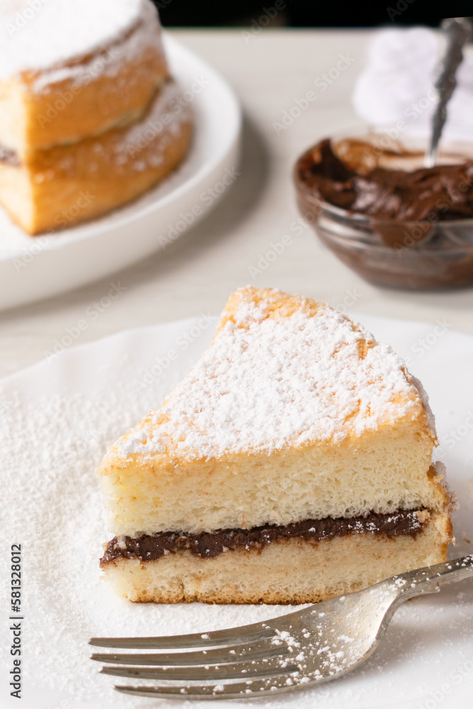 Angel Cake filled with hazelnut spread and garnished with powdered sugar, on a white plate and white background. Angel Cake filled with hazelnut spread and garnished with powdered sugar, on a white plate and white background.