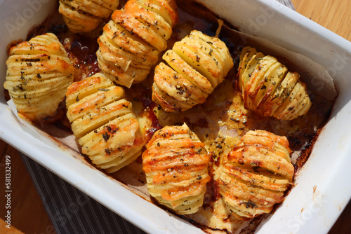 Hasselback baked Potatoes with fresh herbs and garlic in a white baking dish. Traditional swedish food