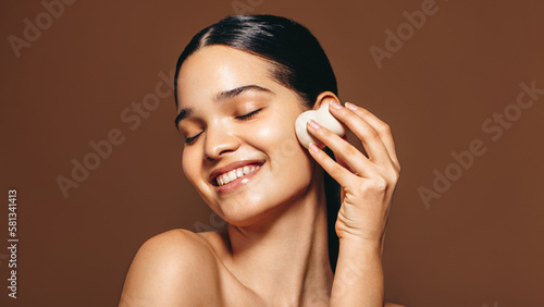 Skincare with a beauty blender; woman applies a facial product on her perfect skin