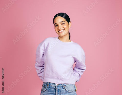 Female in her 20s looking at the camera in a studio, standing against a pink background