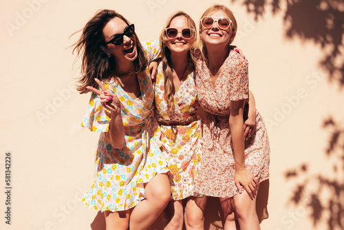 Three young beautiful smiling hipster female in trendy summer dresses  clothes. Sexy carefree women posing in the street. Positive models having fun, talking, chatting. Going crazy. In sunglasses photo