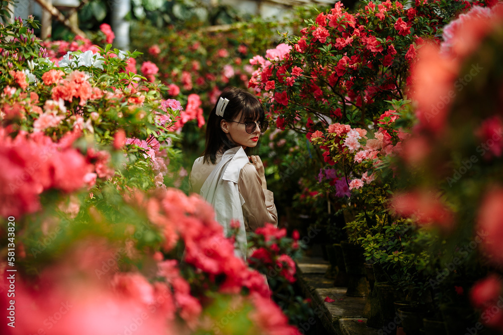 Girl in sunglasses and cream dress in a garden of azaleas