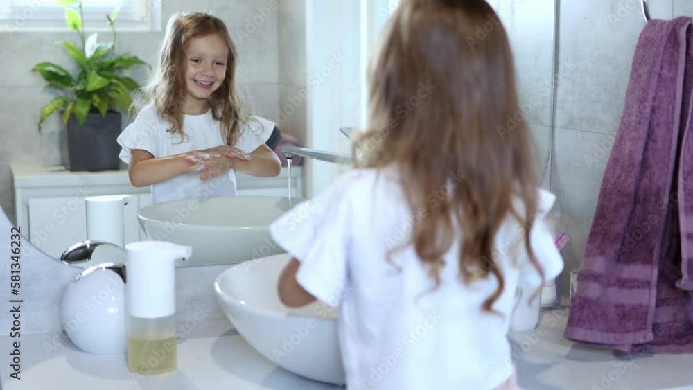 Girl in the washroom. A little girl 4-5 years old washes her hands by herself, standing in front of a large mirror. Children's hygiene. 4k footage. Girl in the washroom. A little girl 4-5 years old washes her hands by herself, standing in front of a large mirror. Children's hygiene. 4k footage.