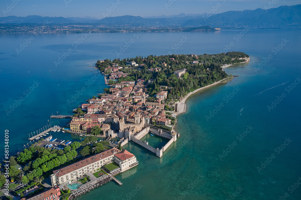 Aerial view of Sirmione, an ancient village on southern Garda Lake. Scaligero Castle drone view. Italian castles Scaligero on the water.  Popular travel destination on Lake Garda in Italy. - obrazy, fototapety, plakaty 
