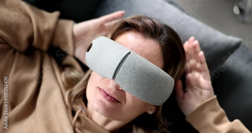 Tired woman puts massage glasses on eyes lying on couch photo