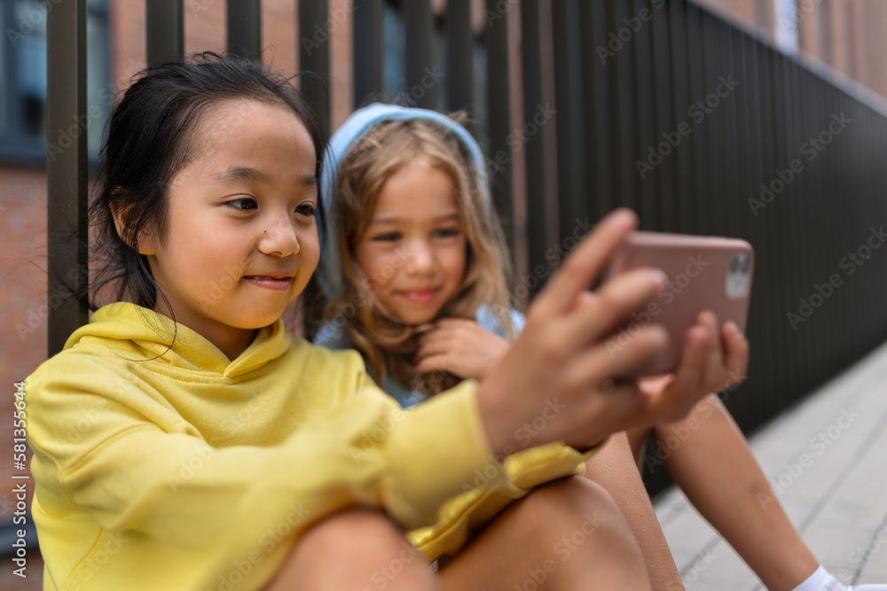 Little girls with hood sitting in sidewalk and scrolling smartphone. Little girls with hood sitting in sidewalk and scrolling smartphone.
