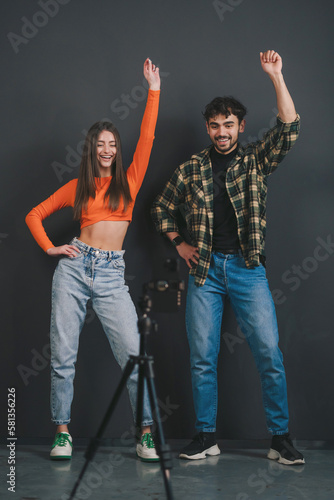 Excited couple recording dance video clip for social media using cell phone on tripod, doing dance moves on black wall background. Internet challenge authentic