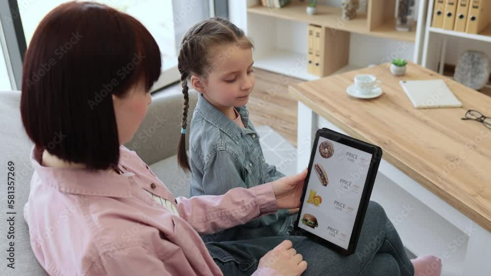 Close up of smiling shoppers choosing fast food at discount on delivery webpage while relaxing at home. Serene woman and girl spending quality time together while buying precooked meals via tablet. Close up of smiling shoppers choosing fast food at discount on delivery webpage while relaxing at home. Serene woman and girl spending quality time together while buying precooked meals via tablet.