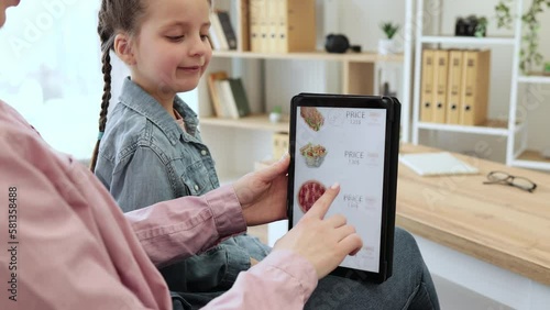 Close up of smiling shoppers choosing fast food at discount on delivery webpage while relaxing at home. Serene woman and girl spending quality time together while buying precooked meals via tablet. photo