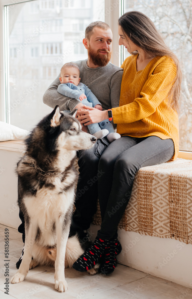 Family with baby boy sitting on the bed with cute dog. Mother and father with their son and doggy together smiling. Beautiful parenthood time. Pet with owners Family with baby boy sitting on the bed with cute dog. Mother and father with their son and doggy together smiling. Beautiful parenthood time. Pet with owners