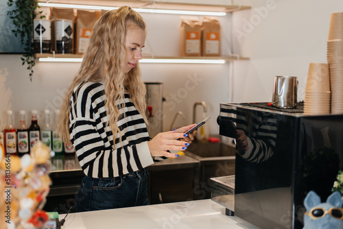 Portrait of smiling waitress barista using mobile phone at work