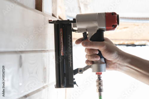 Unrecognizable builder worker hand using pneumatic stapler for wooden board. Framework making, hardwood stitching work photo
