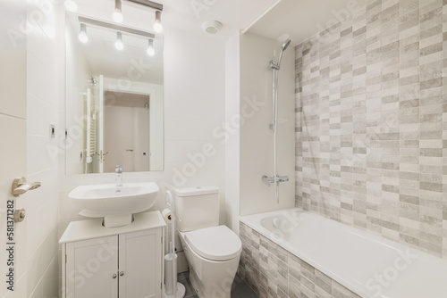 White clean bathroom with tiled tub, sink and toilet with mirror. Concept of cleanliness and simple but modern design in a private house or apartment. Copyspace