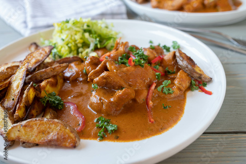 Chicken with paprika cream sauce, potato wedges and salad on a plate. Closeup