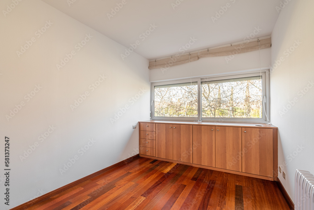 Obraz premium Light and compact empty room with dark wood laminate and a closet near the windows with blinds. Concept of hotel room or an empty apartment after being handed over by the developer