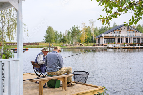Anglers catch fish with fishing rod in specially equipped convenient place on lake. Leisure and lifestyle