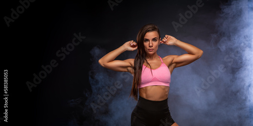 Young woman in sportswear smiling. Muscular fitness model on a black background with smoke. sports girl
