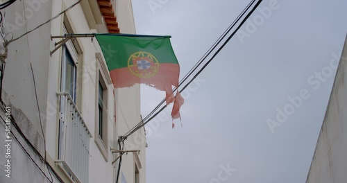 Tattered flag of Portugal blowing in the wind in an alleyway in Nazare, Portugal. photo