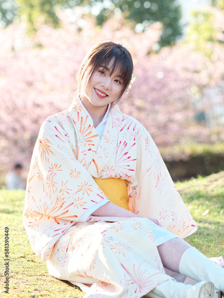 Portrait of beautiful young Chinese girl in Japanese kimono sitting on meadows with blossom cherry flowers background in spring garden, beauty, emotion, lifestyle, expression and people concept. Portrait of beautiful young Chinese girl in Japanese kimono sitting on meadows with blossom cherry flowers background in spring garden, beauty, emotion, lifestyle, expression and people concept.