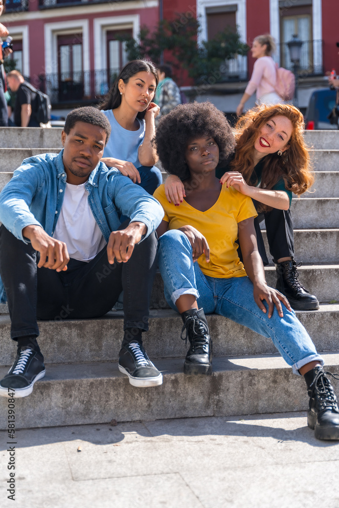 Obraz premium Portrait of happy multiethnic friends sitting on stairs in the city, young models