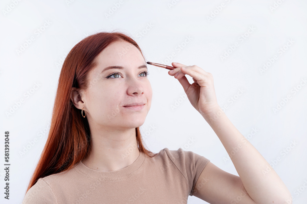 Joyful redhead young woman using makeup brush making up isolated on white background Joyful redhead young woman using makeup brush making up isolated on white background