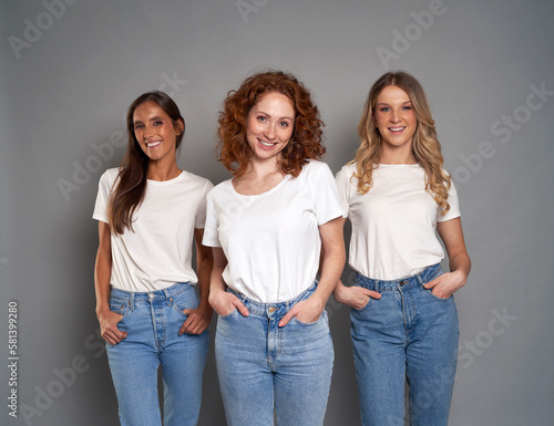 Portrait of three young caucasian women wearing blue jeans and white tshirt on grey background
