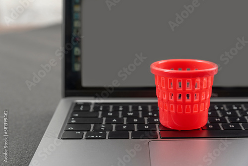 Miniature toy trash can on laptop keyboard. Concept of deleting files and cleaning up information garbage. Cleaning and maintenance of laptop.