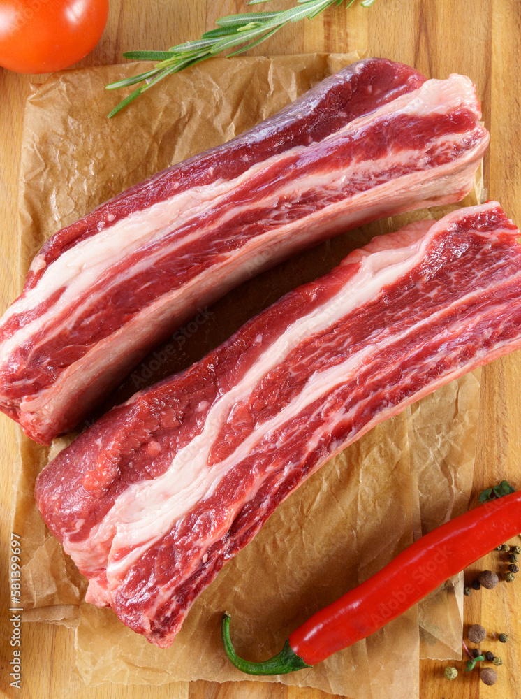 Raw Tomahawk steak on wooden background with spices. Cooking meat. Vertical photo
