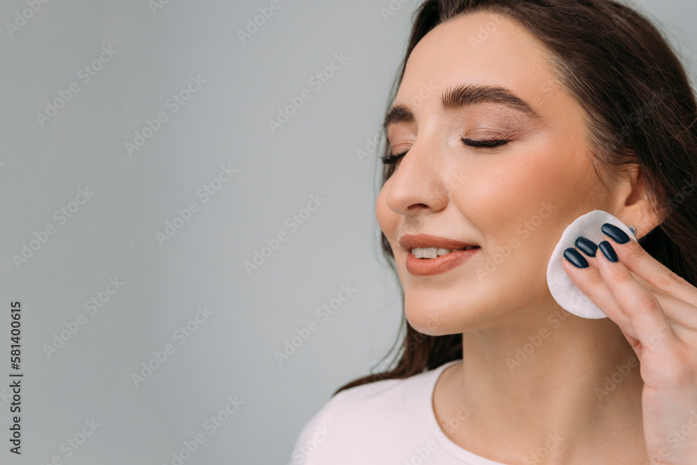 young dark-haired girl removes makeup from her face with a cotton pad, copy space young dark-haired girl removes makeup from her face with a cotton pad, copy space