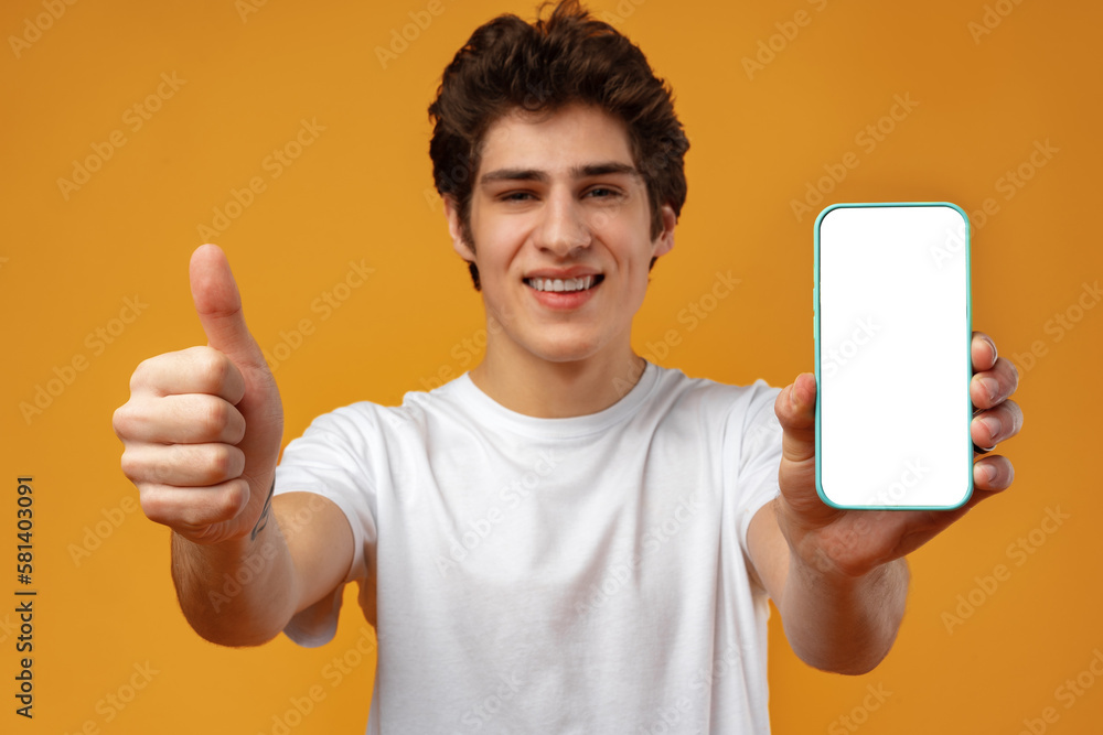 Smiling young man showing mobile phone blank white screen mockup to camera. Smiling young man showing mobile phone blank white screen mockup to camera.