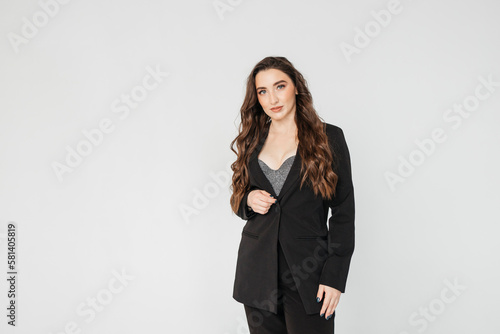 young businesswoman with long curly hair in a black suit stands on a white background
