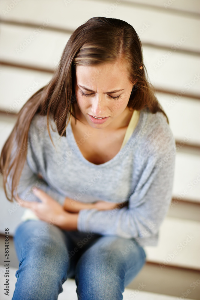 Feeling the emptiness grow inside. an unhappy young woman sitting on a staircase holding her stomach. Feeling the emptiness grow inside. an unhappy young woman sitting on a staircase holding her stomach.