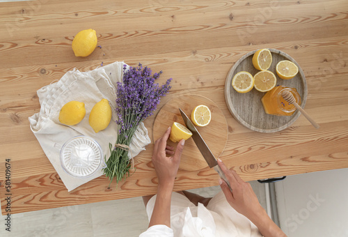 Young woman cutting lemon on wooden board. Preparation of fresh llemonade. photo