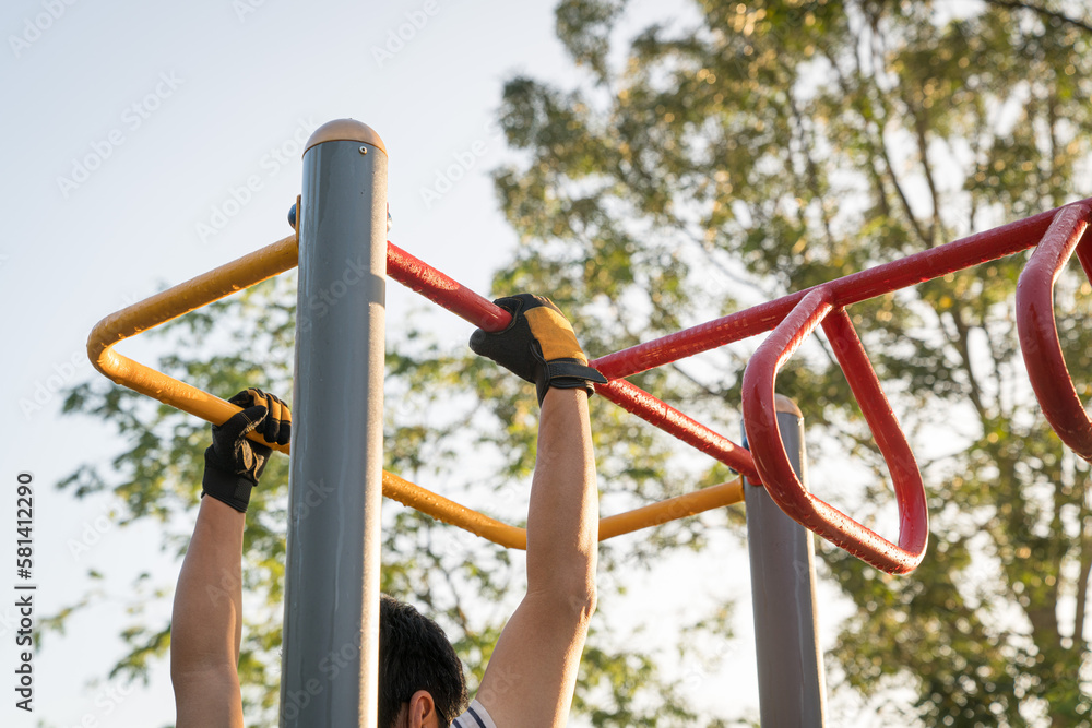 Man working out outdoors, arms swinging on monkey bar. Strength training or fitness exercise concept.