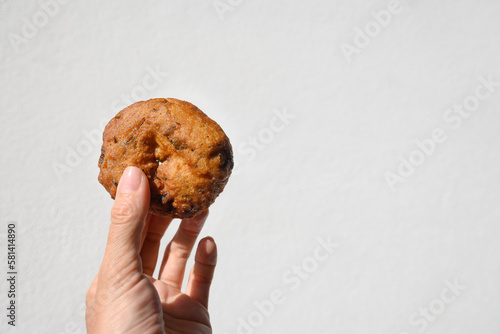 Ulundu Wade spicy lentil fritters made of dhal, onion, chilli, curry leaves. One Ulundu wade in female hand on white background. India and Sri Lanka street food. Close up. Copy space. photo