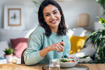 Beautiful smiling woman eating healthy while looking at camera at home.