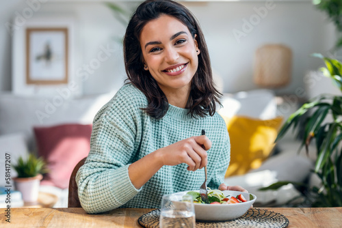 Beautiful smiling woman eating healthy while looking at camera at home.
