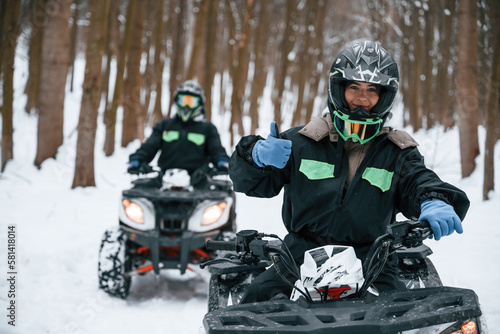 Woman with her friend. Two people are riding ATV in the winter forest