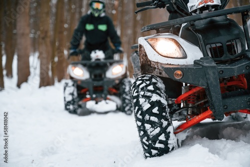 On the snowy ground. Two people are riding ATV in the winter forest