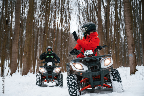 Man is looking behind at his friend. Two people are riding ATV in the winter forest