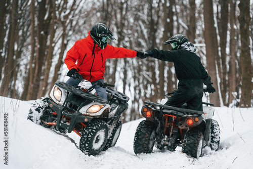 Knocking the fists. Two people are riding ATV in the winter forest