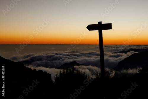 Destination travel sign on the tourist trail in the mountains. Sunset over the clouds on background,