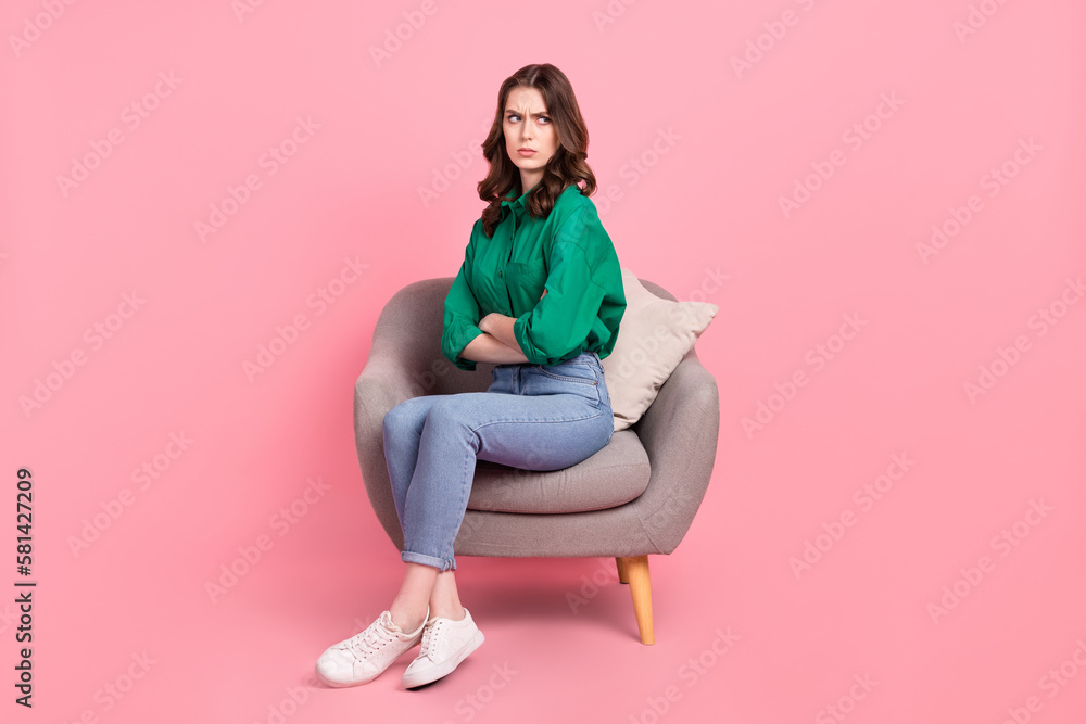 Full size photo of offended unhappy girl dressed green shirt sit on armchair.offendedly look at empty space isolated on pink background