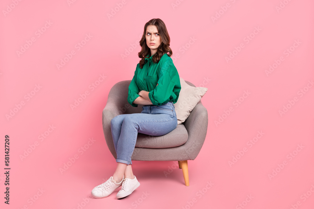 Full size photo of offended unhappy girl dressed green shirt sit on armchair.offendedly look at empty space isolated on pink background Full size photo of offended unhappy girl dressed green shirt sit on armchair.offendedly look at empty space isolated on pink background