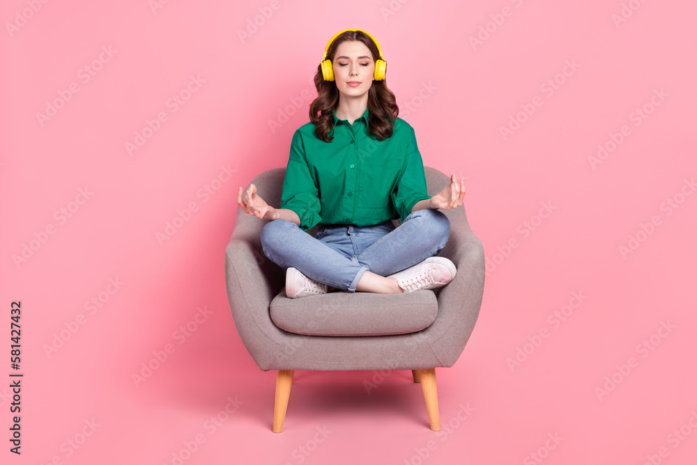 Full size photo of restful girl dressed green shirt sit on armchair in meditation pose listen relaxed music isolated on pink background Full size photo of restful girl dressed green shirt sit on armchair in meditation pose listen relaxed music isolated on pink background